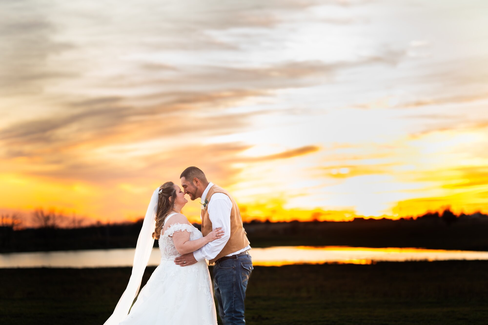Newlyweds kissing by the pond at sunset