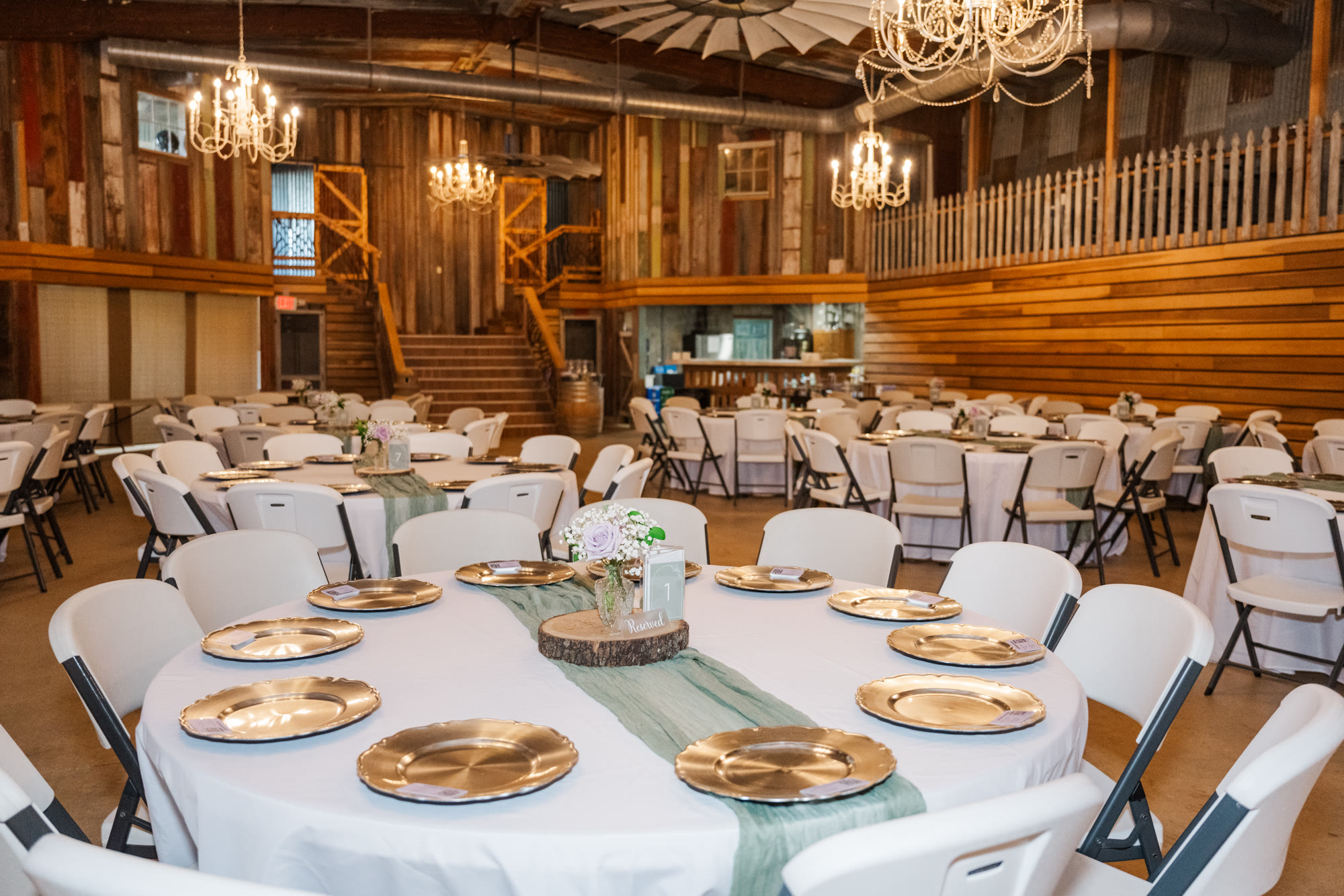 Round tables fully set for a reception in the barn under the chandeliers